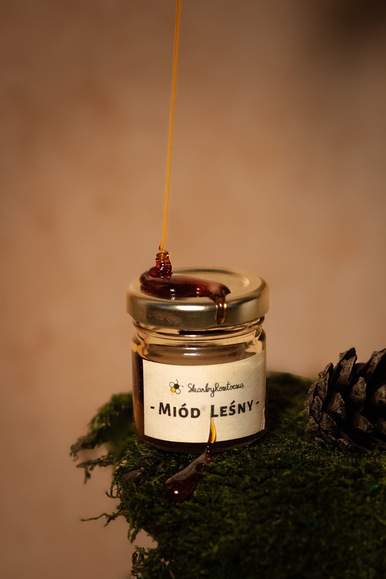Słoik z miodem leśnym na zielonym mchu, z miodem spływającym z pokrywki i spadającym z łyżeczki.