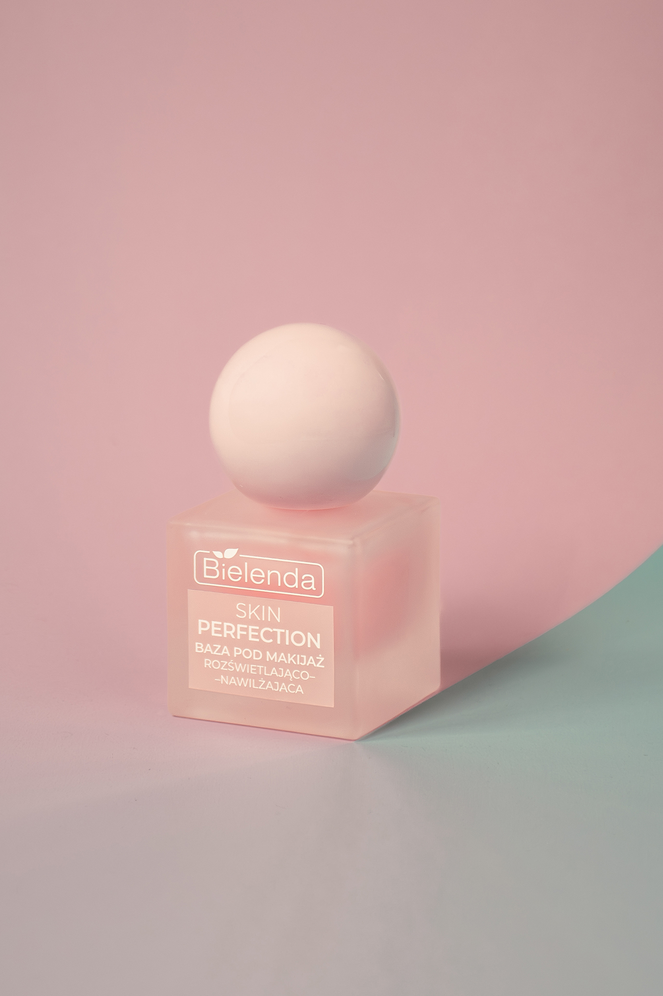 Różowa, matowa butelka Bielenda Skin Perfection baza pod makijaż rozświetlająco-nawilżająca na różowo-niebieskim tle.