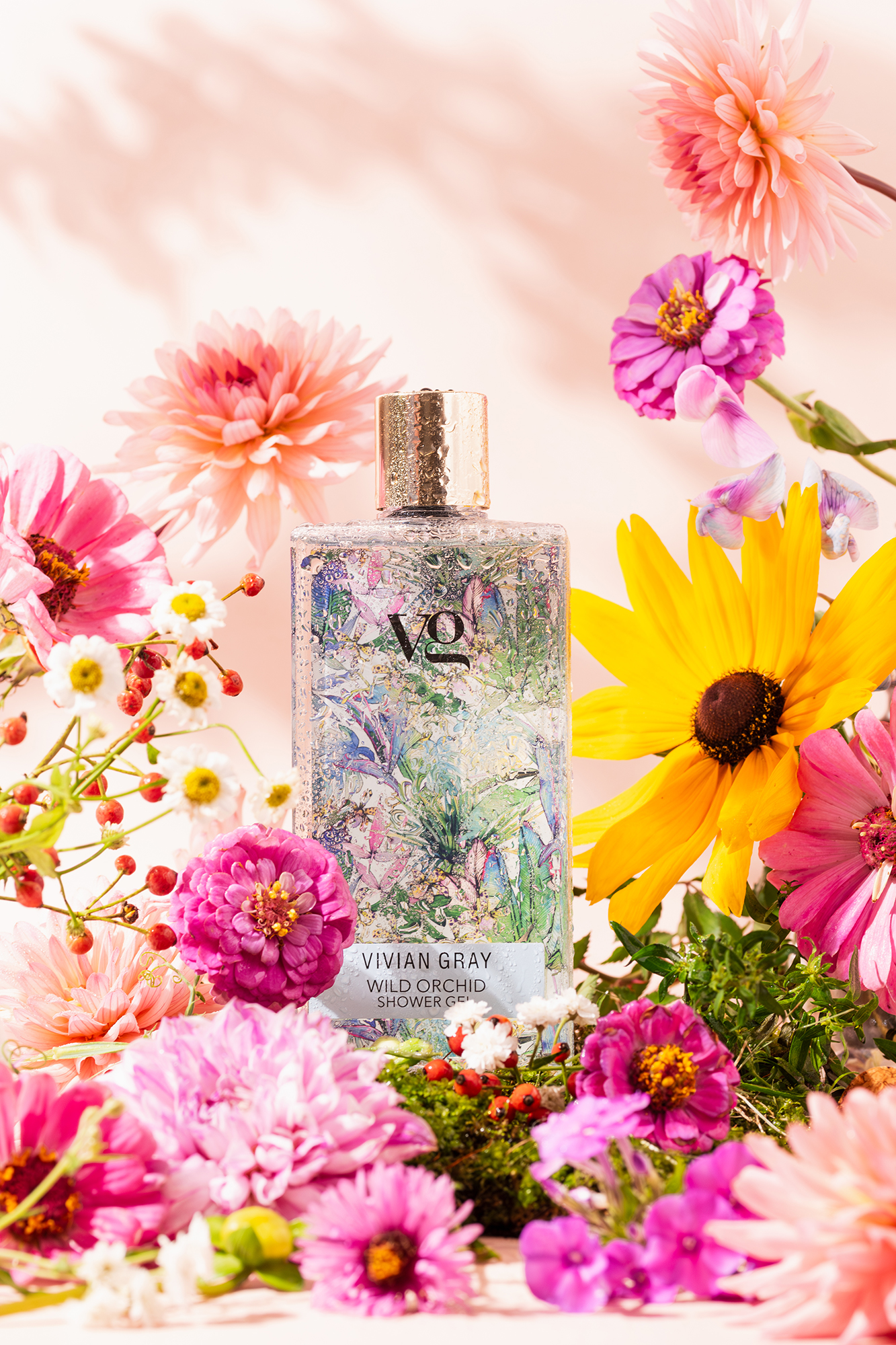 Butelka żelu pod prysznic Vivian Gray Wild Orchid otoczona różnymi kolorowymi kwiatami.