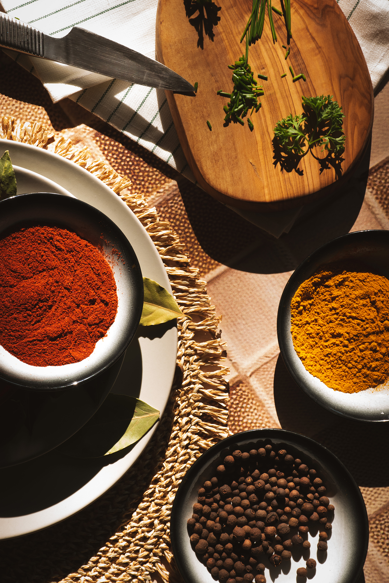 Miseczki z różnymi przyprawami: czerwona papryka, kurkuma i czarny pieprz, obok deska do krojenia z posiekaną natką pietruszki i nożem.
