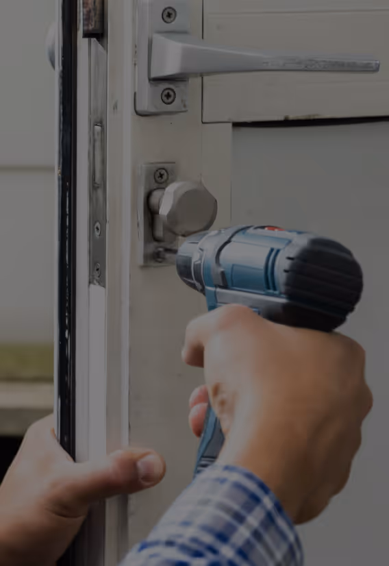 Henkilö käyttää porakonetta asentaakseen tai korjatakseen hopeisen oven lukon valkoiseen oveen.