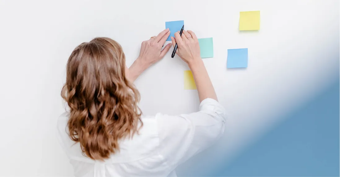 Strategische Marketing-Planung: Eine Beraterin ordnet Gedanken und Prioritäten mit farbigen Post-its an einer weißen Wand.