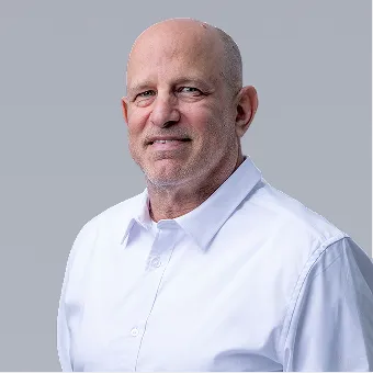 Middle-aged bald man wearing a white button-up shirt against a plain light gray background.
