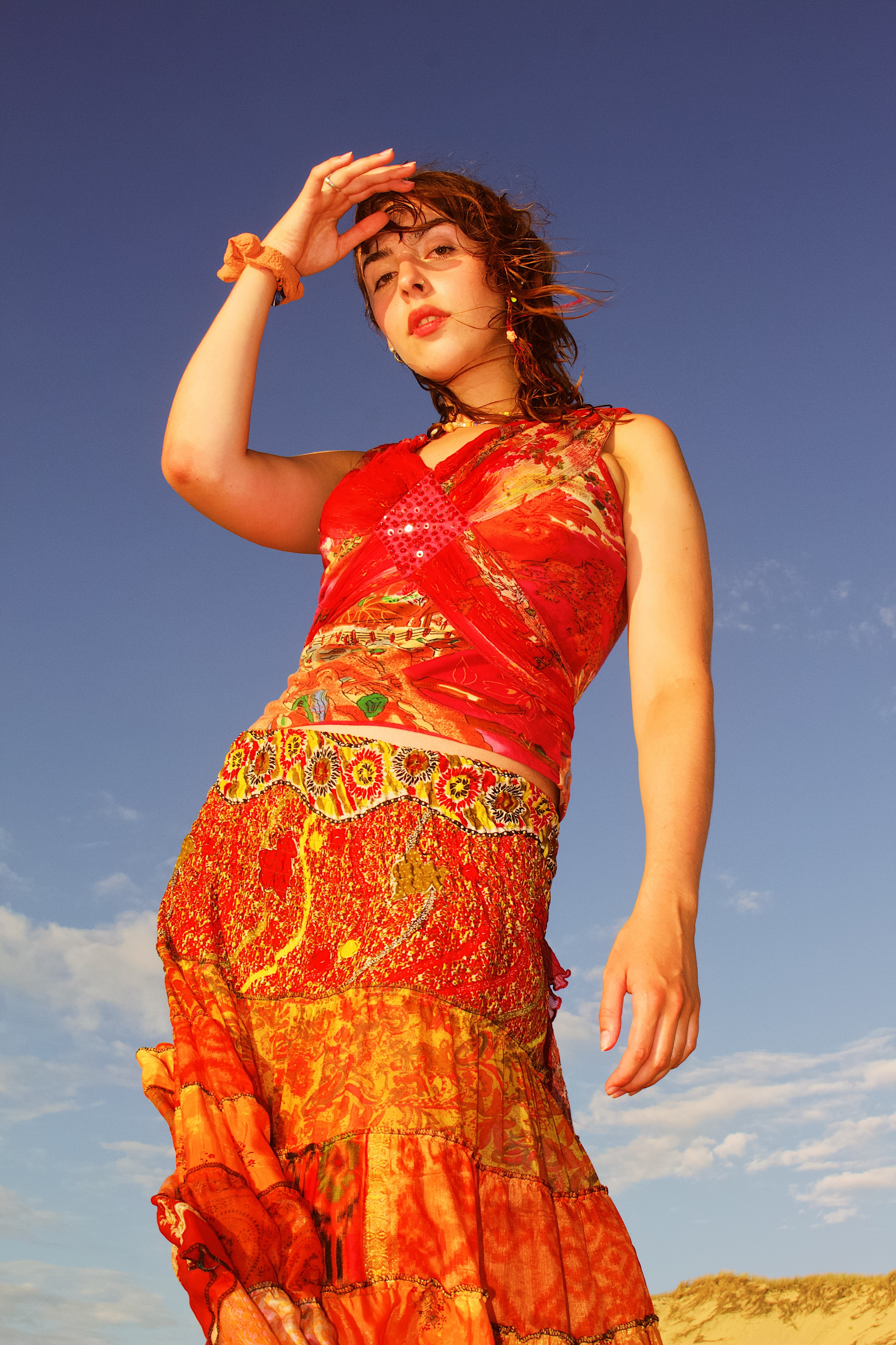 Woman in bright red and orange patterned dress standing outdoors against a clear blue sky.