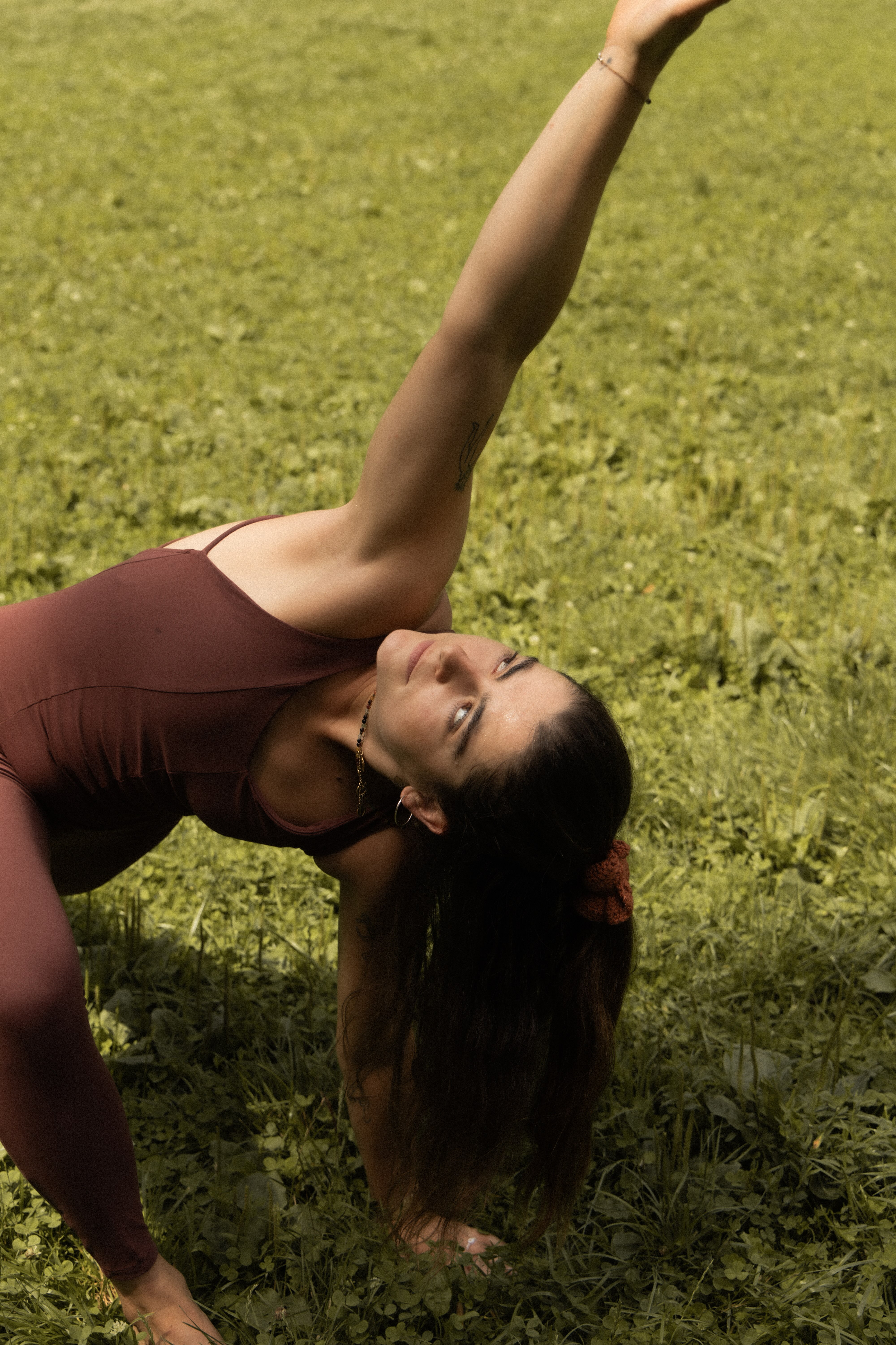 Woman in a maroon outfit performing a yoga pose on green grass outdoors.