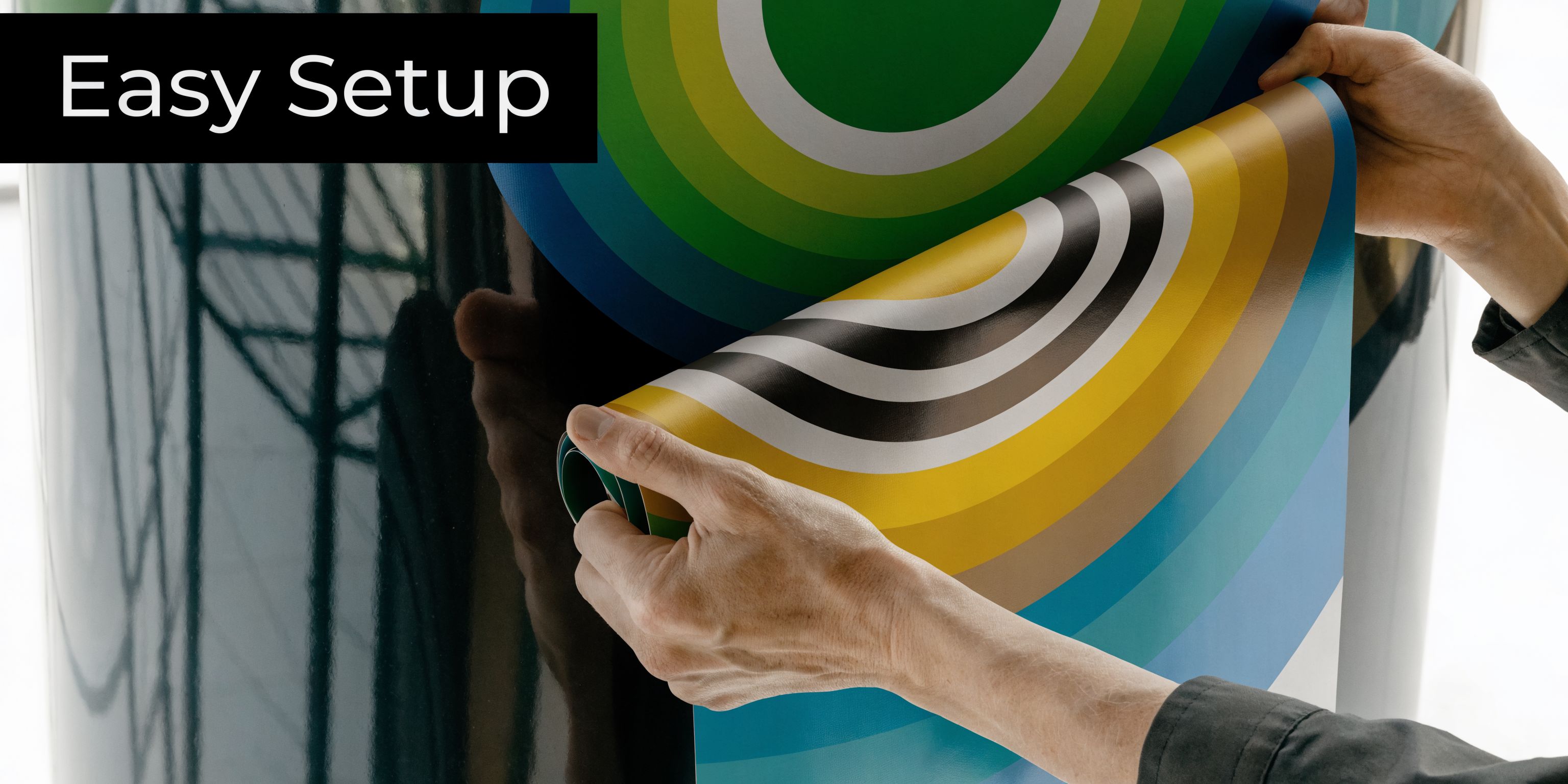 A person applying a colorful circular vinyl adhesive decal onto a large, smooth, dark surface.