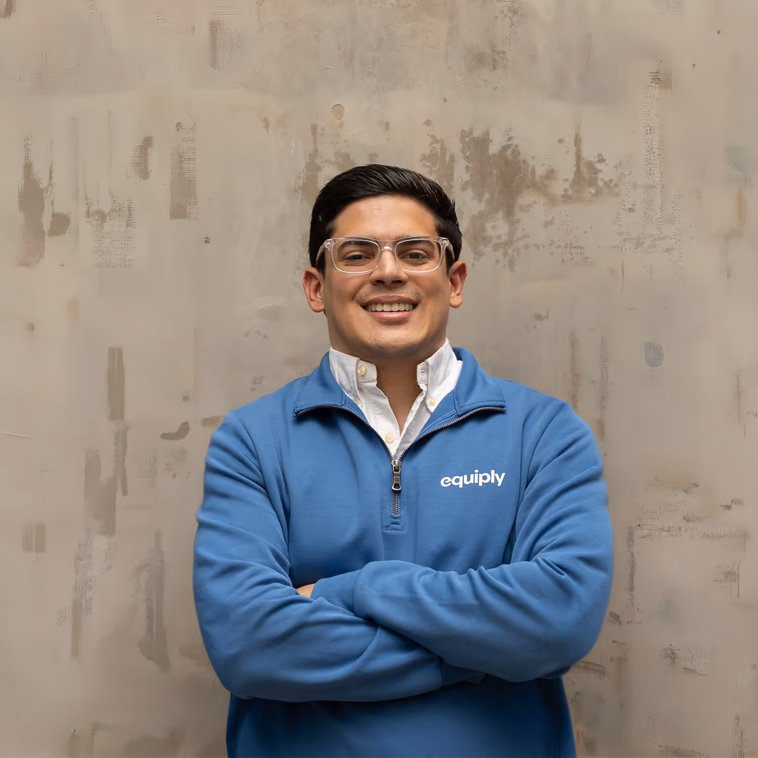 Man with short dark hair and glasses smiling with arms crossed, wearing a blue Equiply sweatshirt over a white collared shirt.