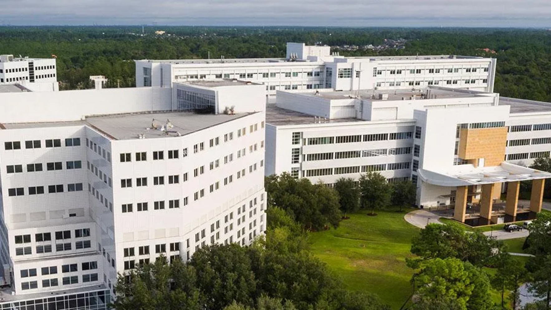 Aerial view of the large white Mayo Clinic hospital complex surrounded by green trees and grass.
