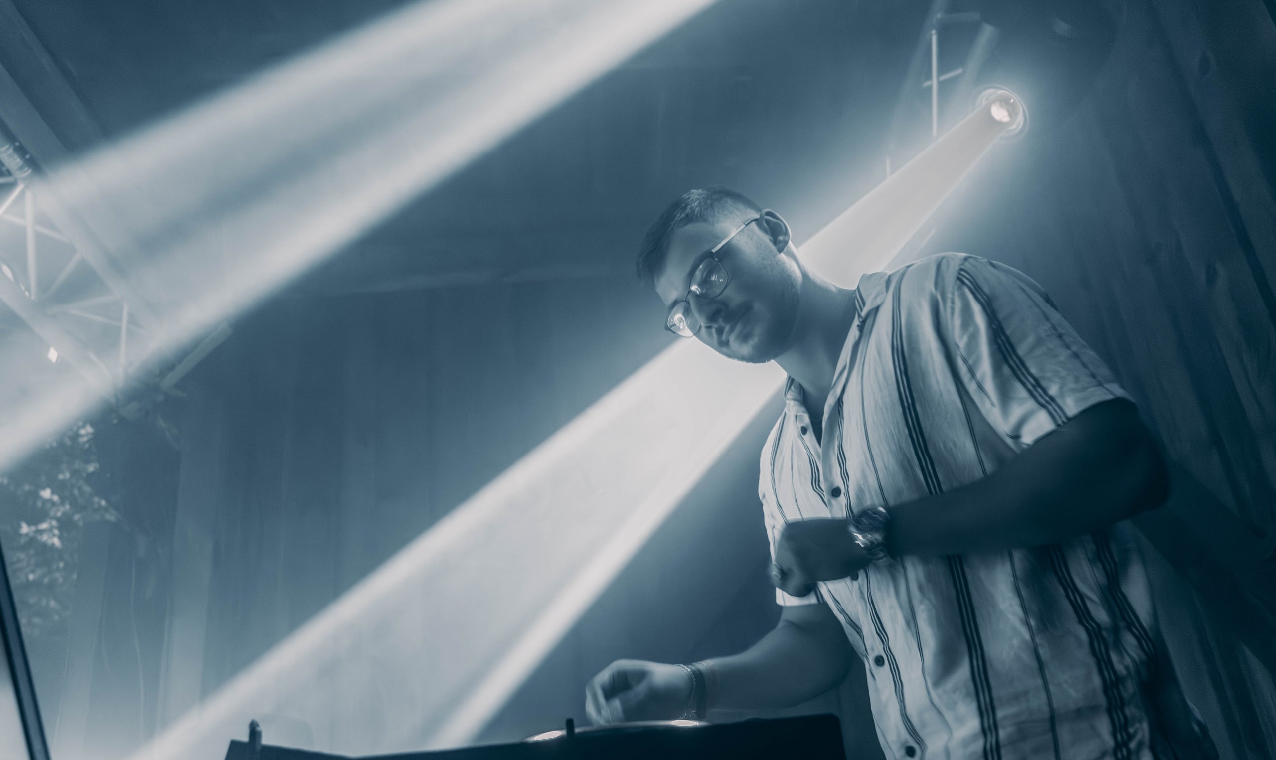 DJ Glen Haens bei einem Live-Clubauftritt, umgeben von blauen Lichtstrahlen und atmosphärischer Bühnenbeleuchtung.