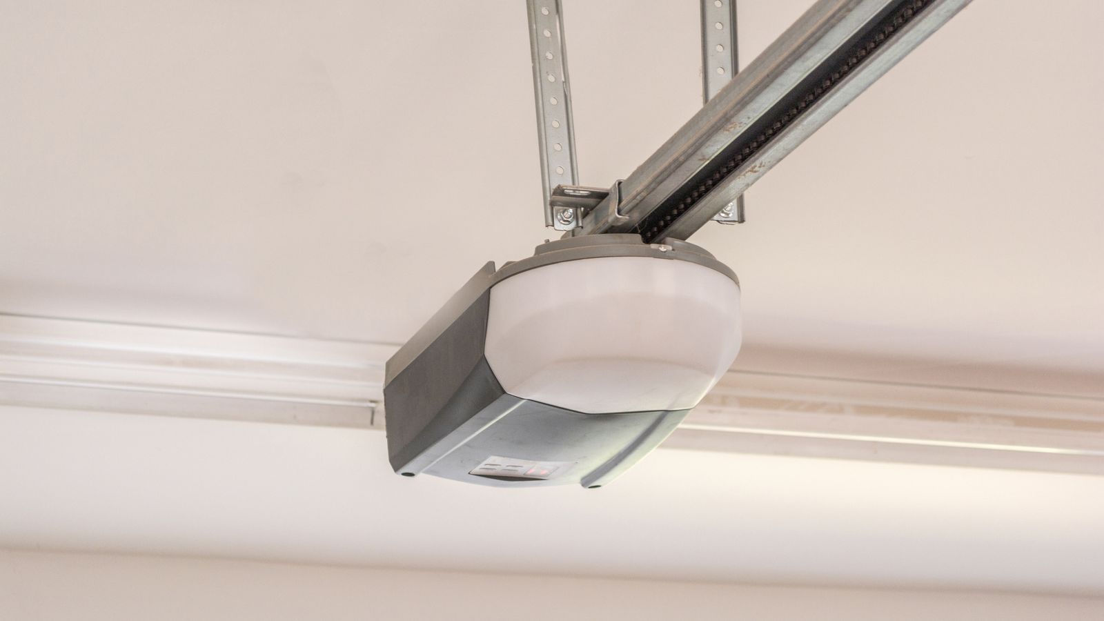 Ceiling-mounted garage door opener motor with metal rail and track system, commonly serviced for repair, installation, or replacement.