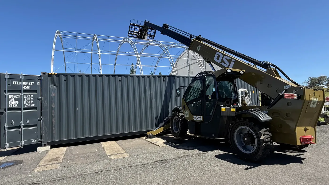 OSI telehandler boom extended over a container tent frame during installation
