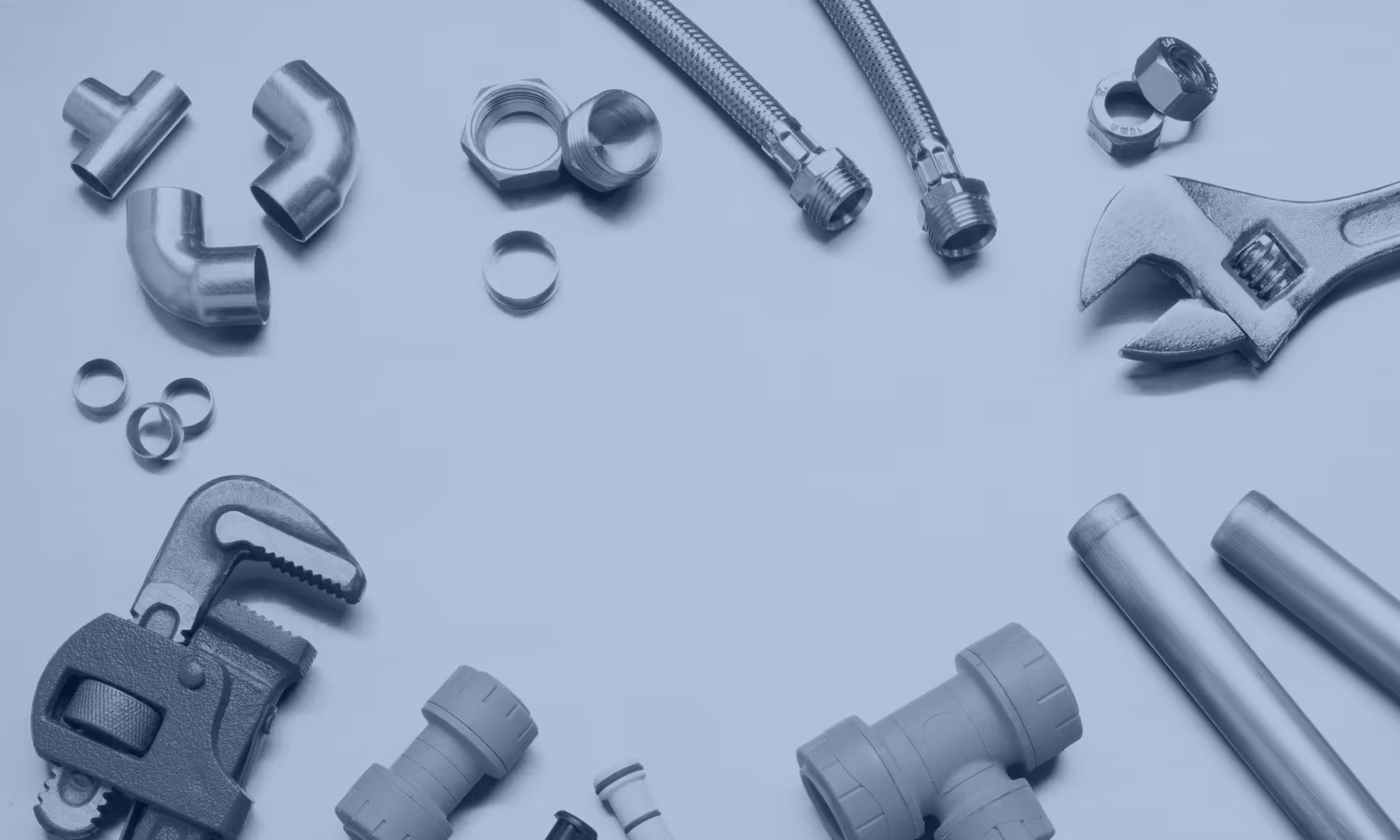 Various plumbing tools and parts including pipe wrench, adjustable wrench, metal pipes, connectors, and flexible braided hoses arranged in a circle on a light surface.