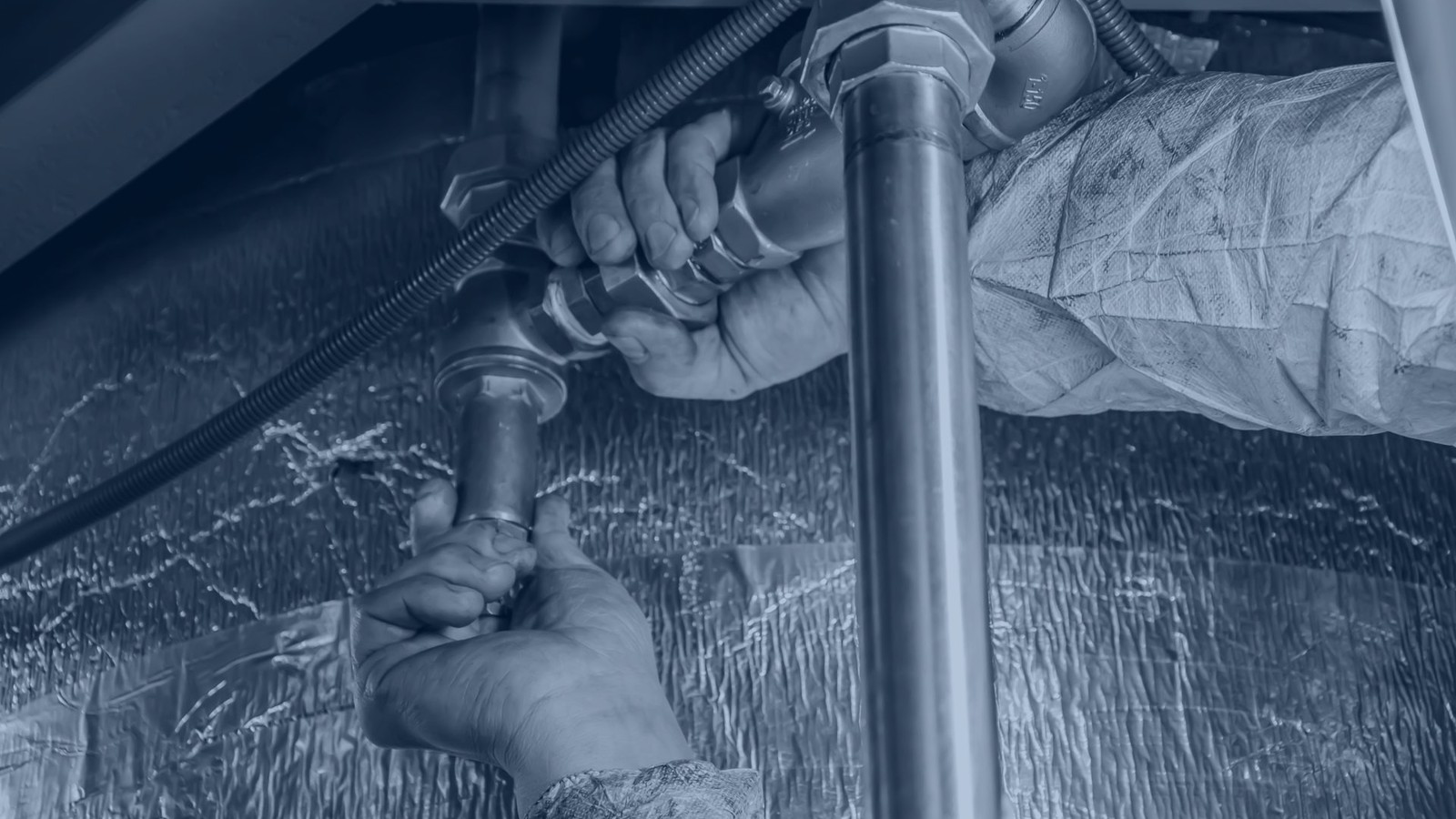 Plumber's hand tools laid out on a workbench, treated with a navy-blue monochrome overlay — Xplore Plumbing blog hero for the Seattle hiring guide