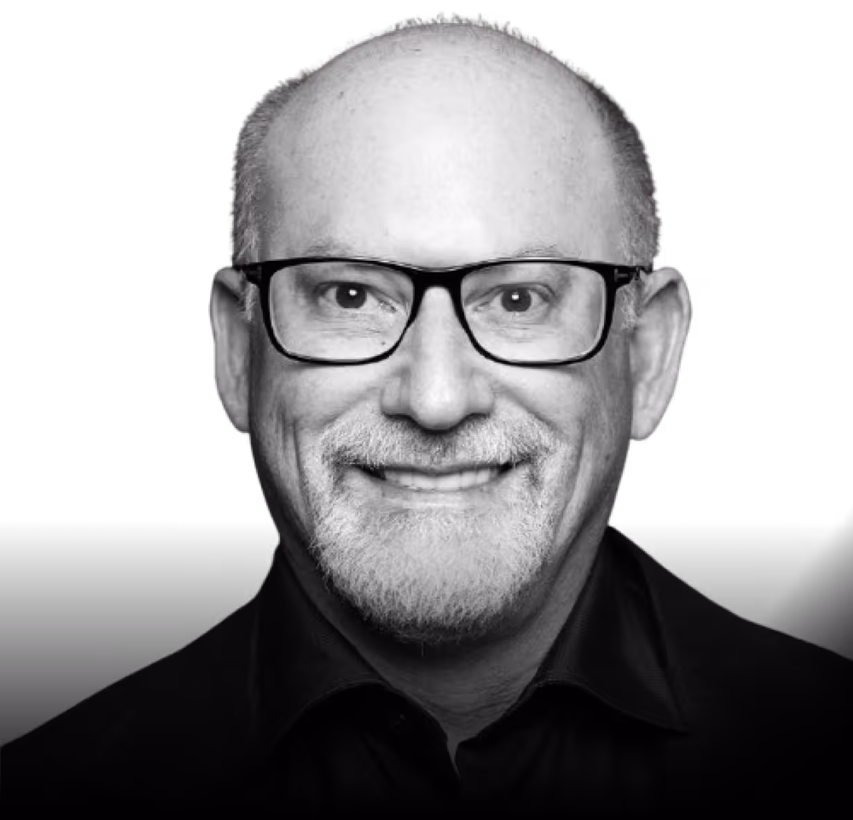 Smiling middle-aged man with glasses, bald head, and a trimmed white beard wearing a dark shirt.