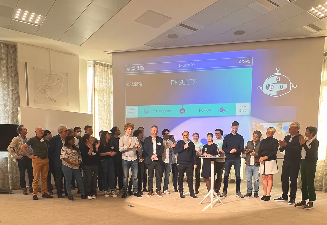 Group of people standing on a stage in front of a screen showing 'RESULTS' for Match 10 between Champions and NukkAI with scores 5238 and 6136.