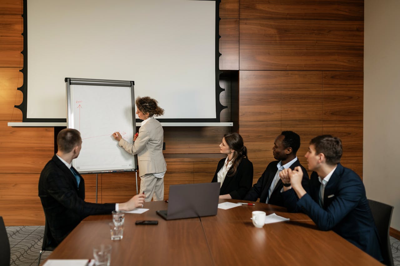 Businesswoman in beige suit presenting with whiteboard to three colleagues seated at a conference table.