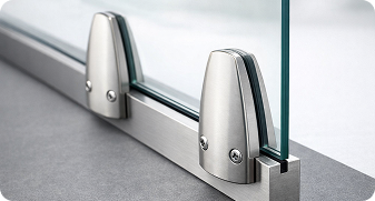Close-up of stainless steel clamps securing a glass panel on a floor surface.