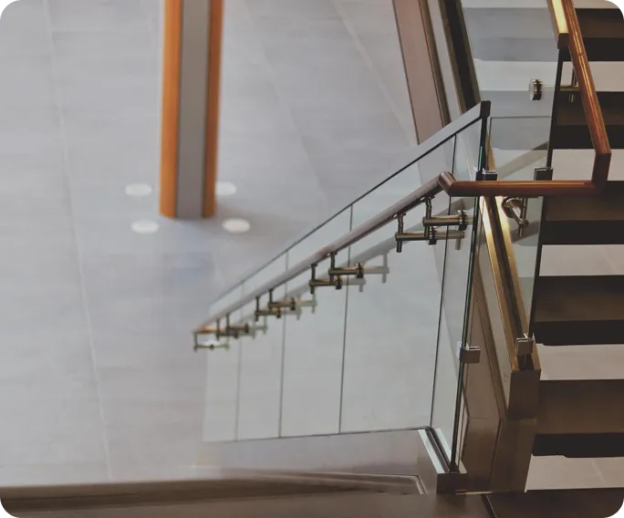 Modern staircase with glass railing and wooden handrail descending to a tiled floor with a vertical wooden pillar.