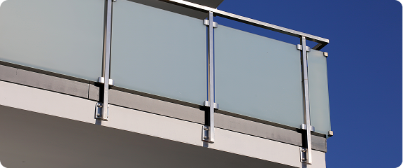 Modern balcony railing with frosted glass panels and metal supports under a clear blue sky.