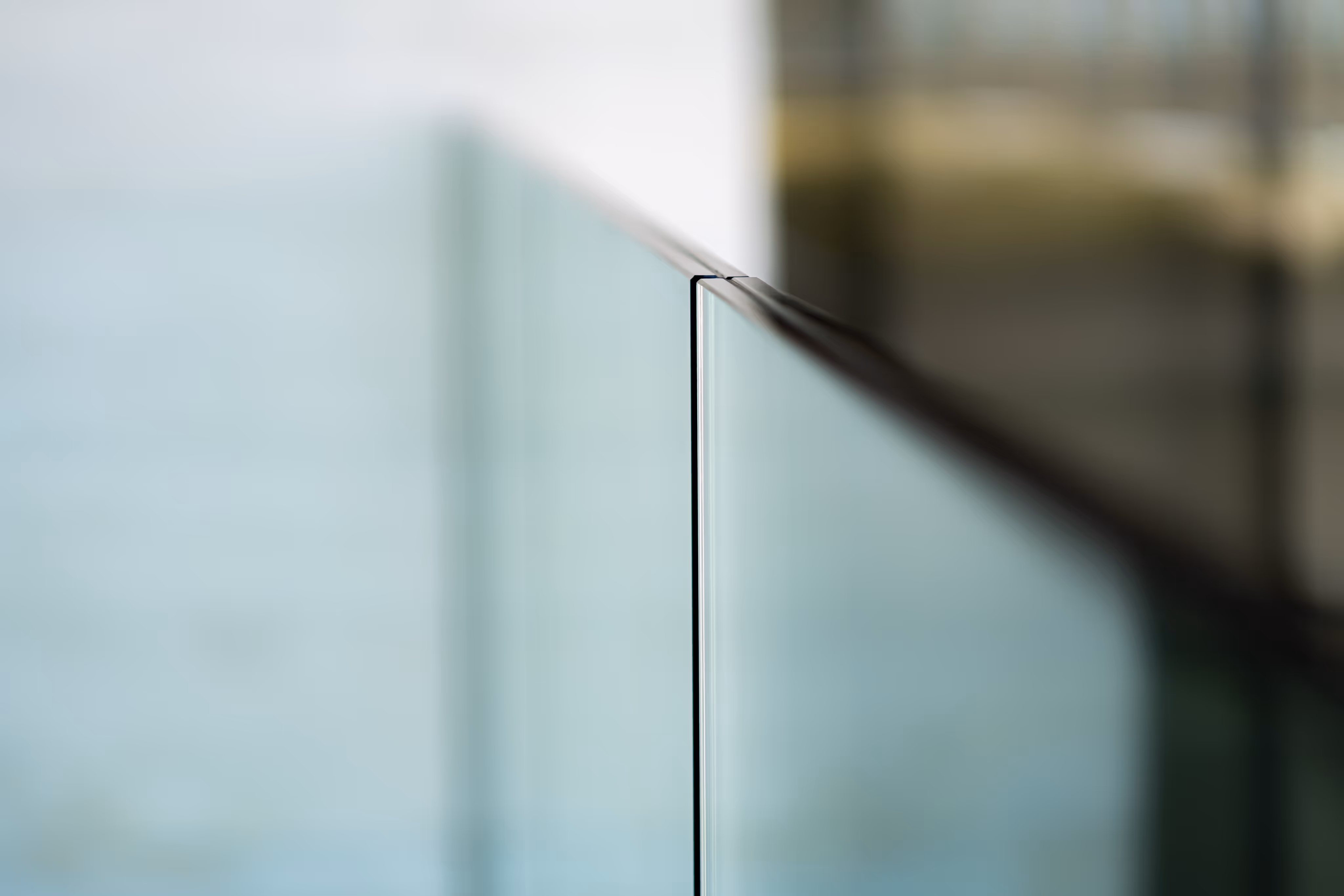 Close-up of a sleek glass railing edge with a blurred background.