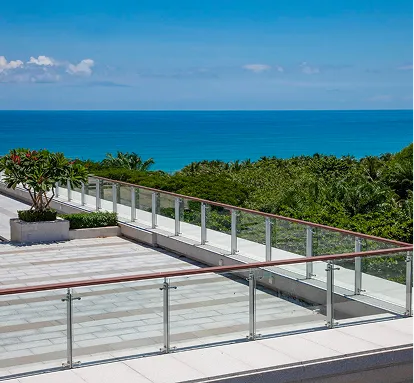 Glass railing terrace overlooking green trees and a blue ocean under a partly cloudy sky.