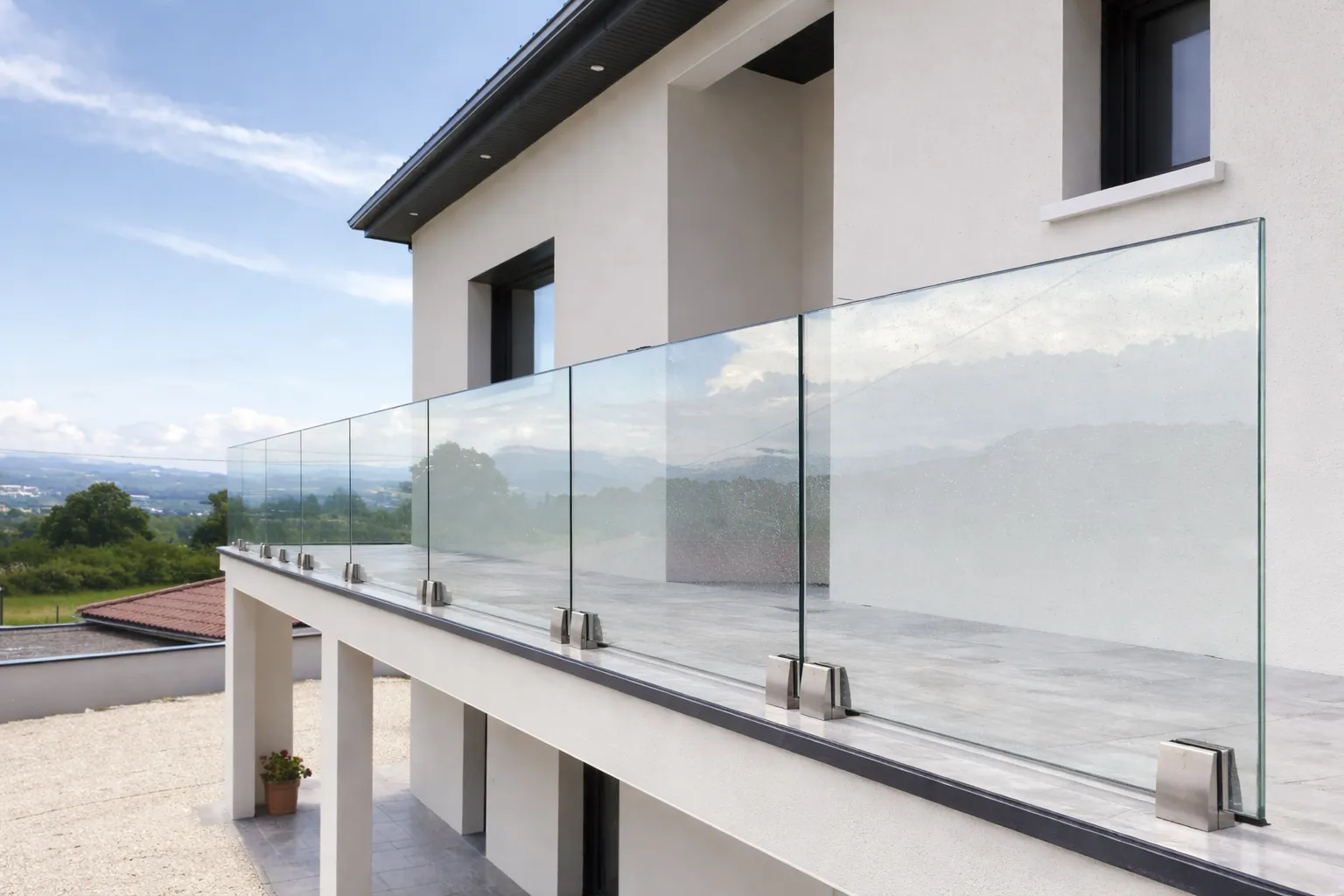 Modern house balcony with transparent glass railing overlooking a green landscape.