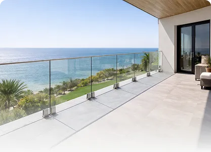Spacious balcony with glass railing overlooking a sunny ocean view and palm trees.
