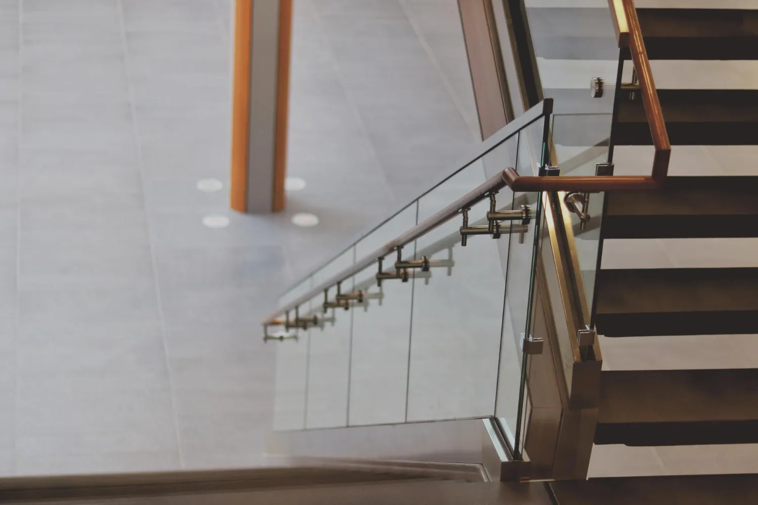 Modern staircase with glass railing and wooden handrail viewed from above.