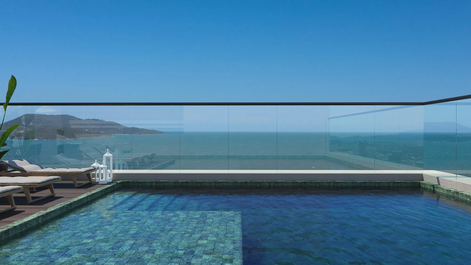Outdoor pool with lounge chairs and glass railing overlooking the ocean under a clear blue sky.