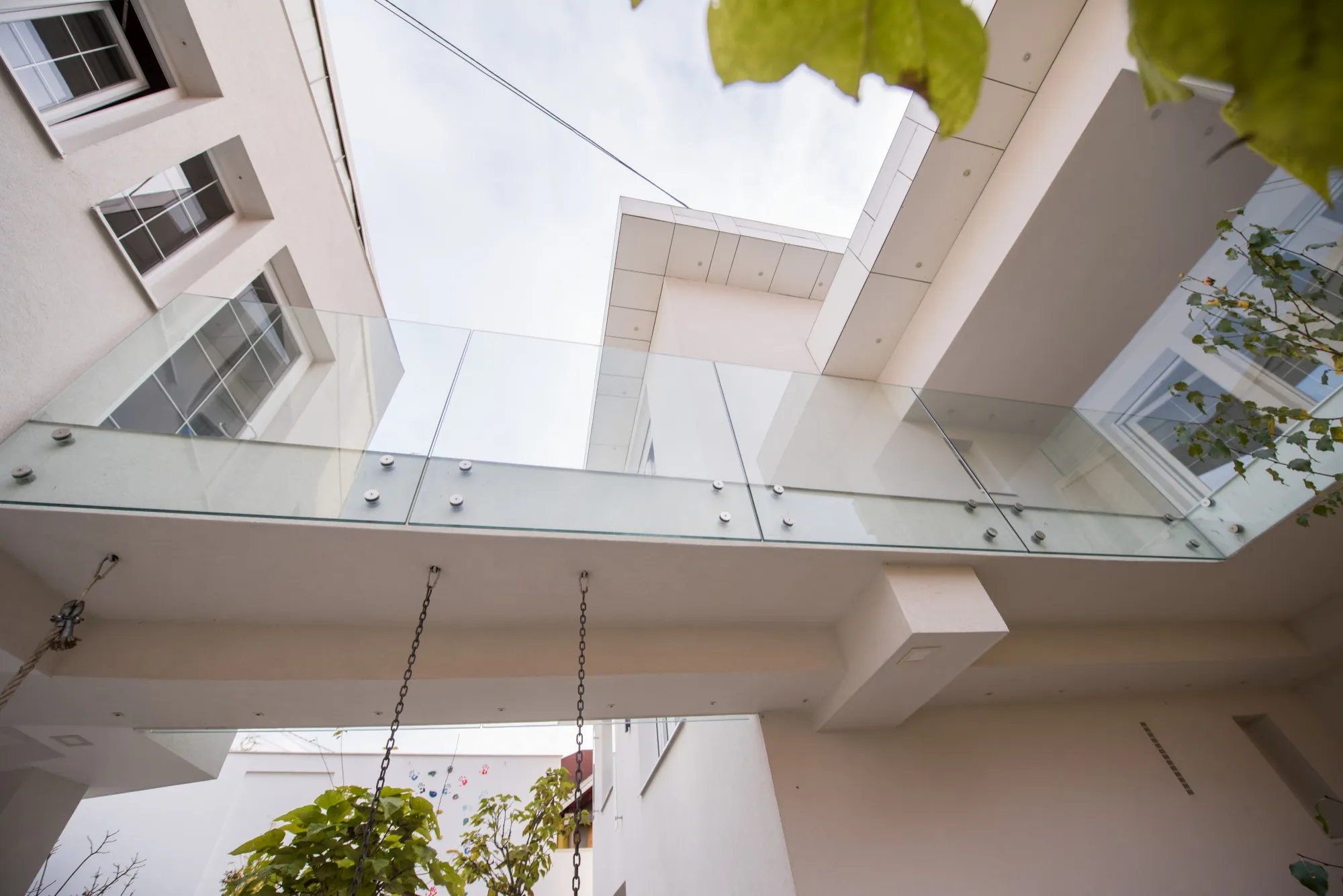 Upward view of a modern building with glass balcony railing and plants below.