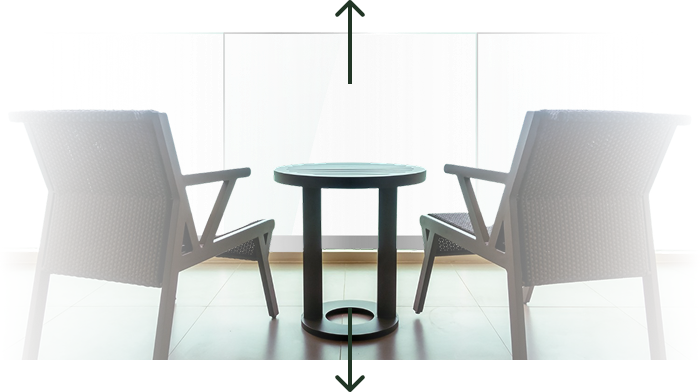 Two modern wicker chairs facing a small round table with large glass windows in the background.