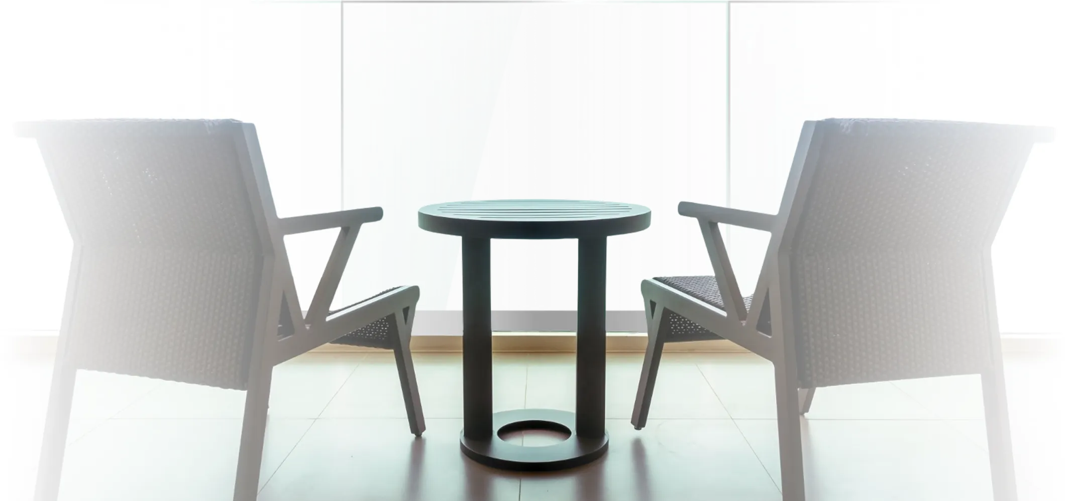 Two modern woven chairs facing each other with a small round black table between them in a bright room.