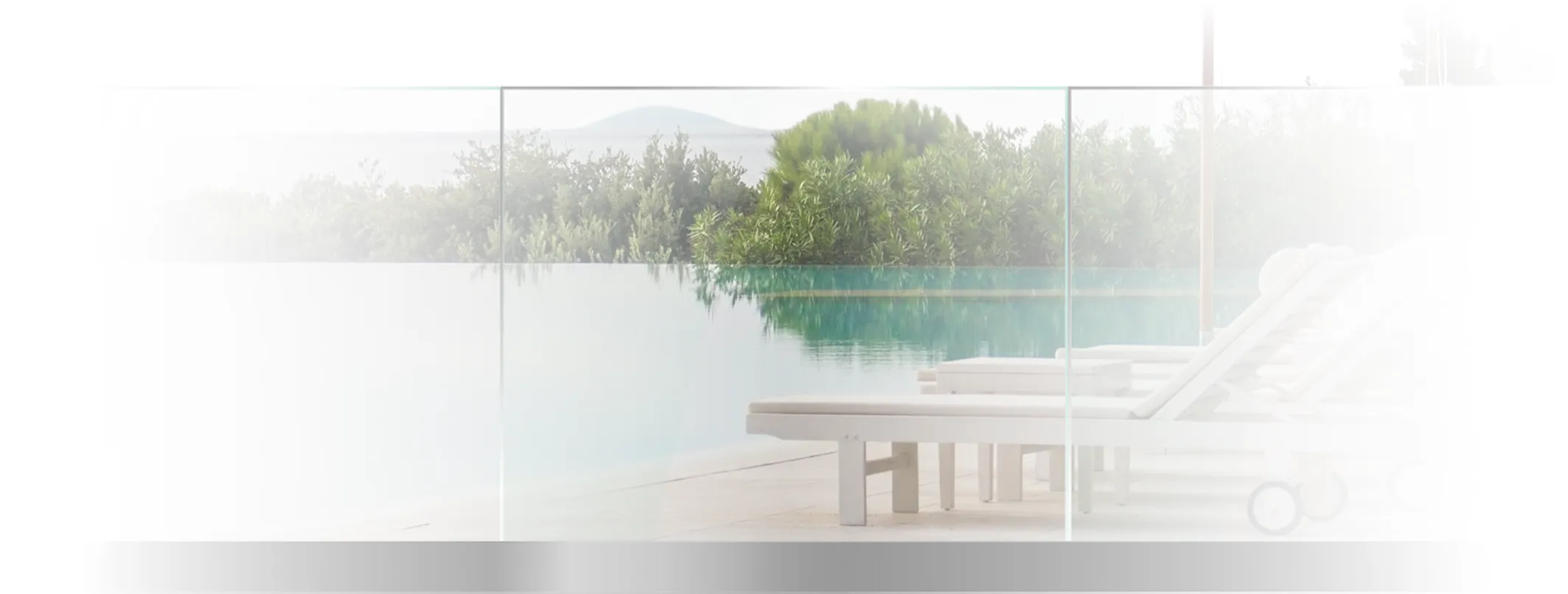 Empty white lounge chairs beside a calm infinity pool with green shrubbery in the background.