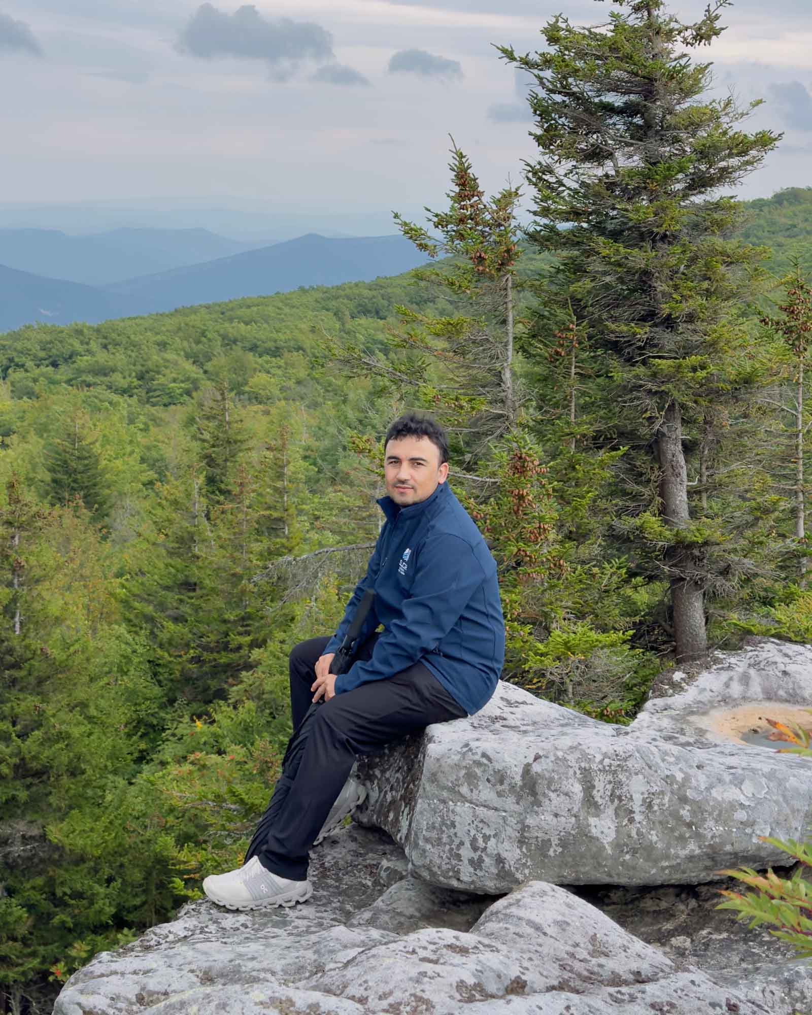 Hassan Ukasha seated on a rock outcrop overlooking a forested mountain range