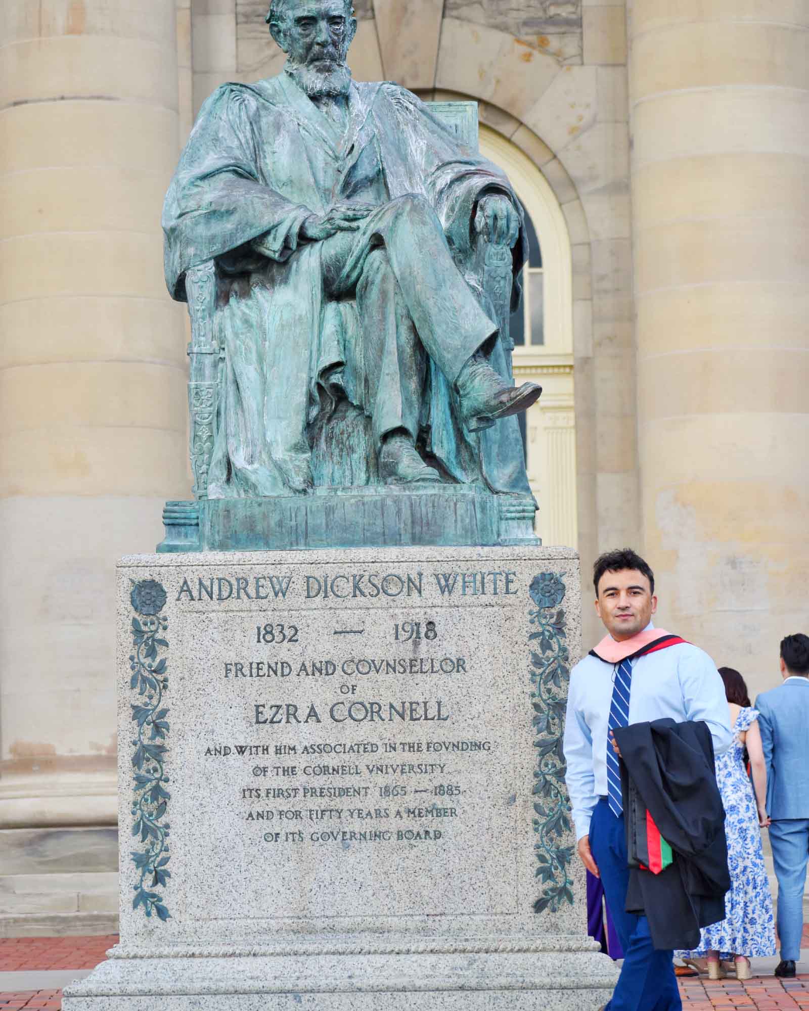 Hassan Ukasha on the Cornell University Arts Quad beside the Andrew Dickson White statue, carrying his graduate gown