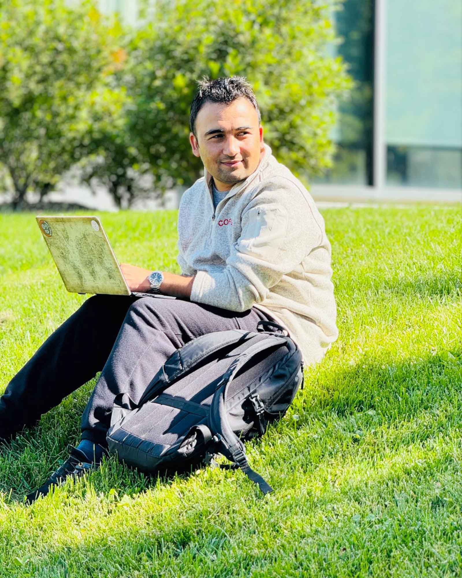 Hassan Ukasha working on a laptop on the Cornell University campus lawn