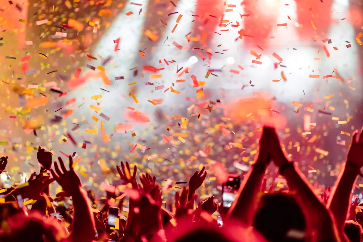 Crowd with raised hands and confetti falling at a lively concert or celebration.