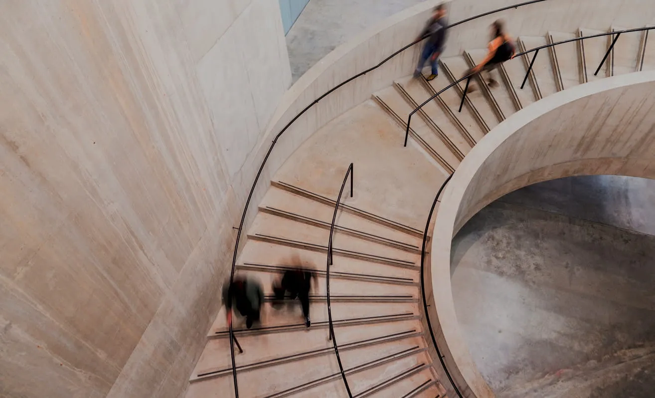 Curved concrete staircase with metal handrails and blurred figures walking up and down.