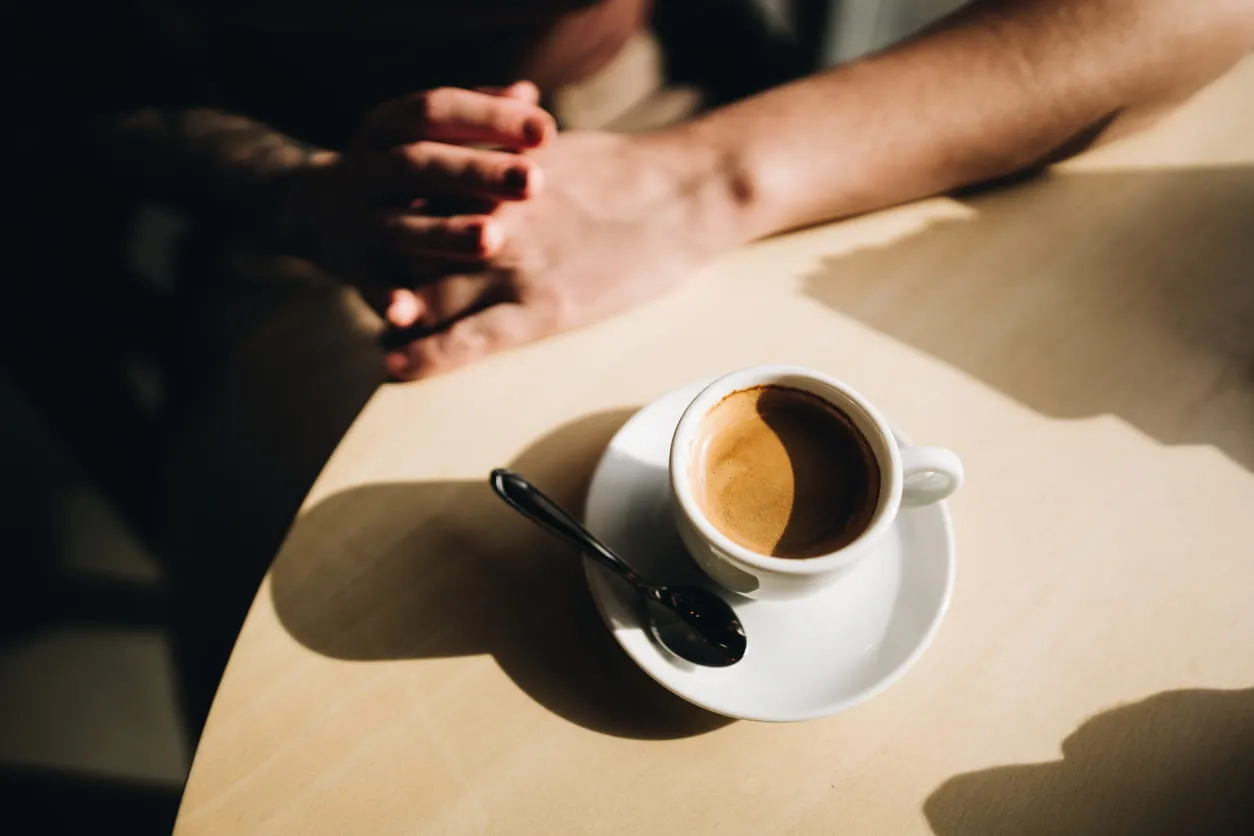 White cup of espresso with a spoon on a saucer on a sunlit table.