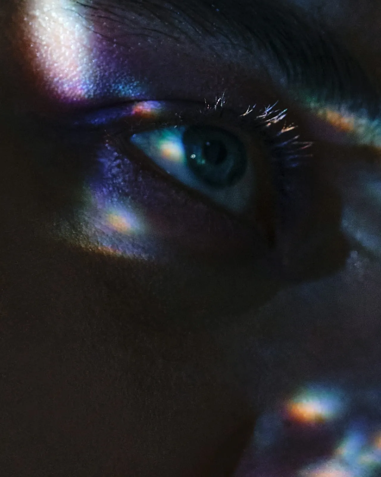 Close-up of a person's eye illuminated by scattered rainbow light patterns on the skin.