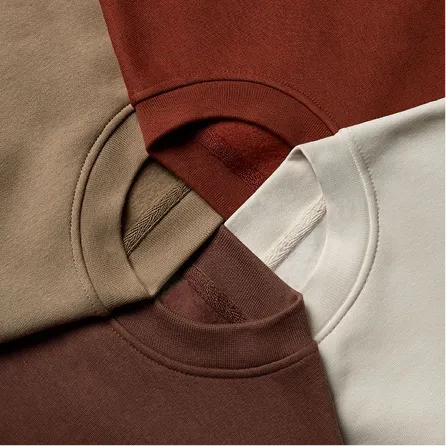 Close-up of four folded crewneck sweatshirts in brown, beige, rust, and off-white colors overlapping in a circular arrangement.