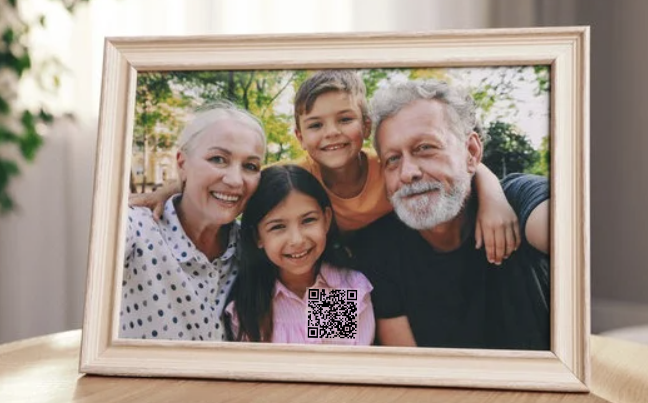 Hand holding a smartphone displaying a gallery app selecting photos, with a framed family picnic photo on a wooden table in the background.