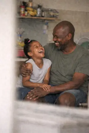 Smiling father and daughter sitting closely, sharing a joyful moment indoors.
