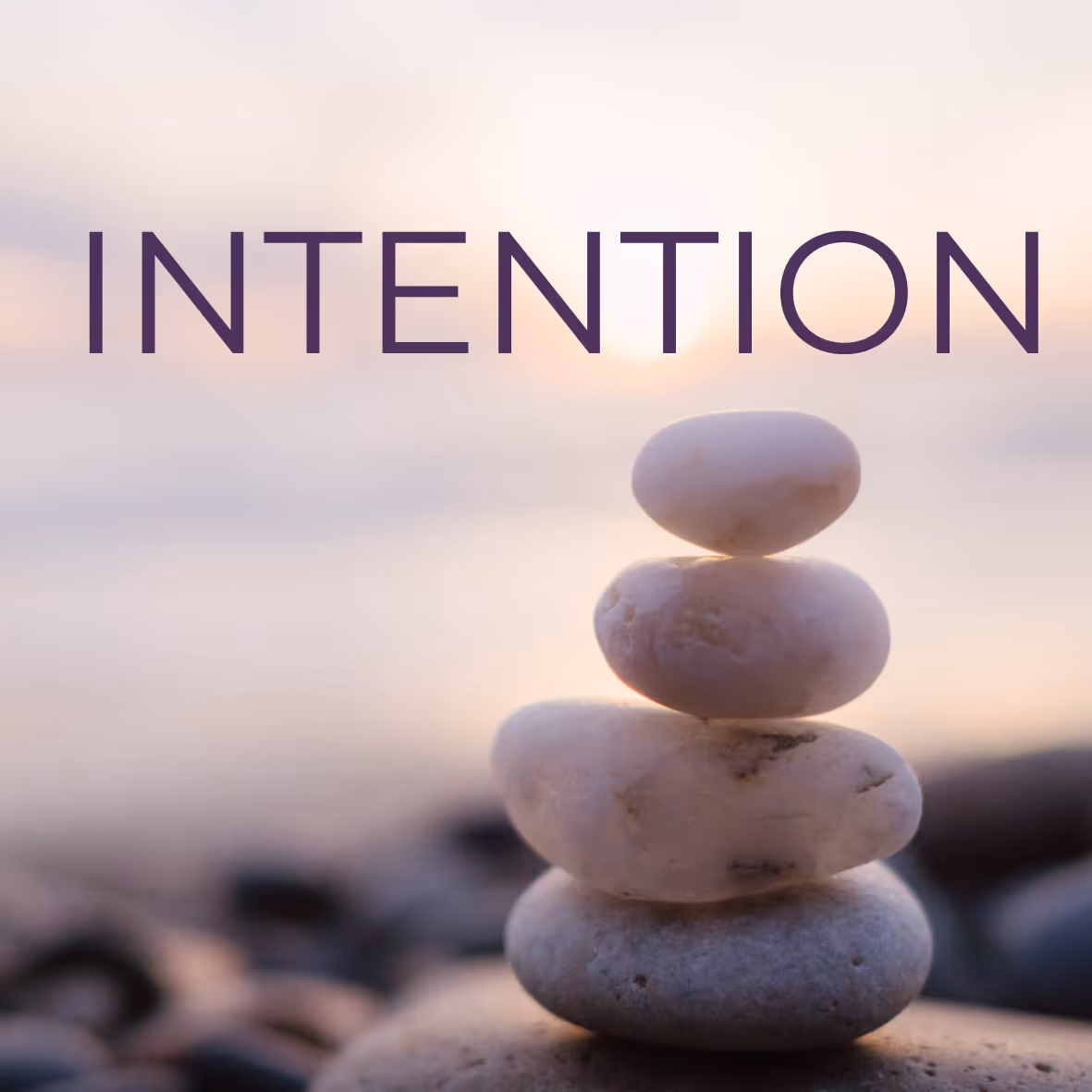 Stack of four smooth white stones balanced with the word INTENTION over a soft, blurred background.