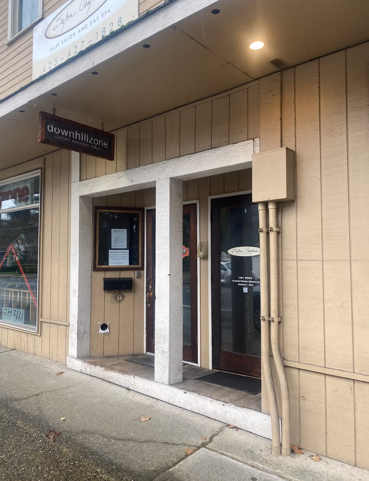 Storefront with two wooden doors under a beige awning; signs indicate a hair salon and a downhill custom mountain bike shop.