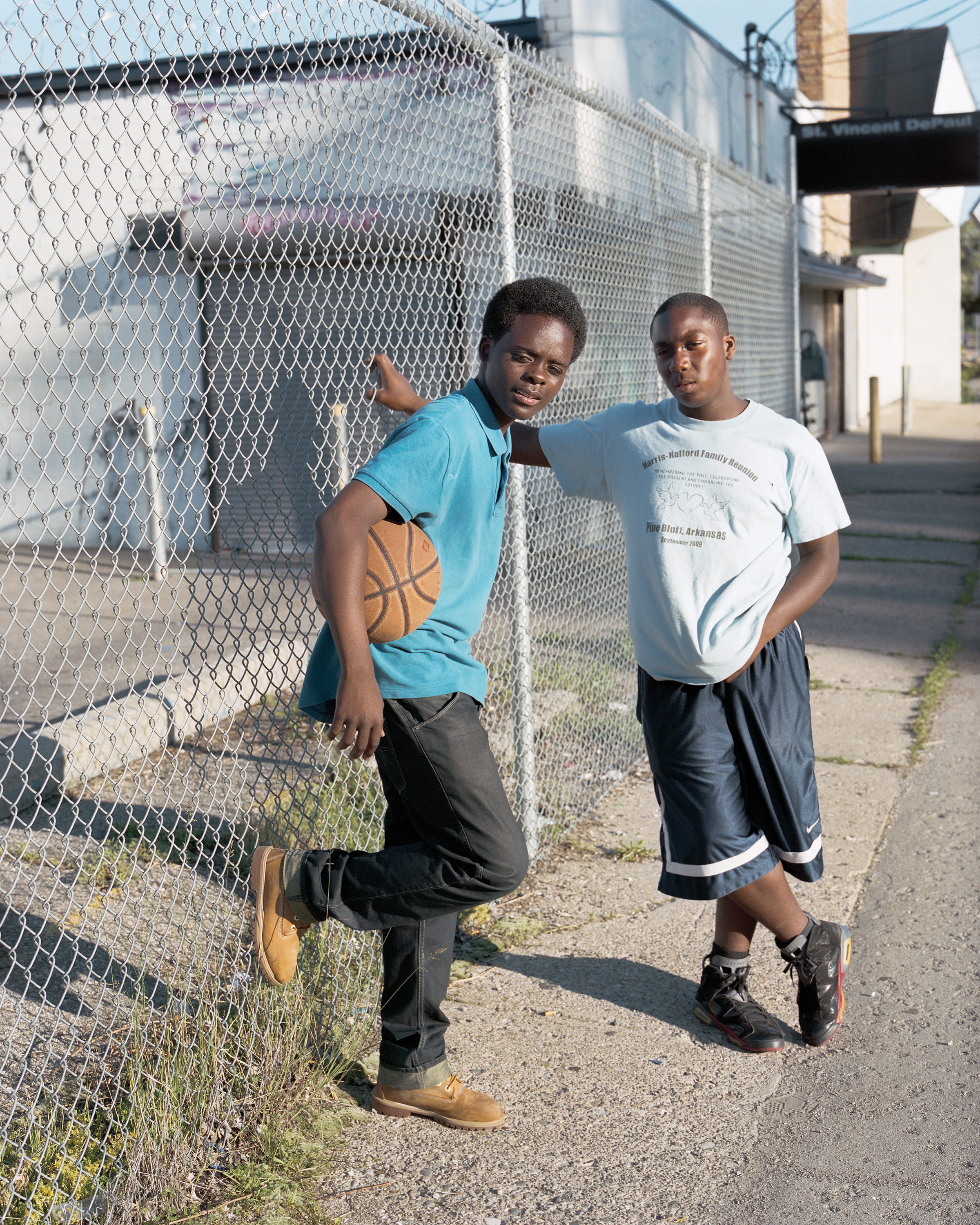 Two teenagers with a basketball lean against a chain-link fence