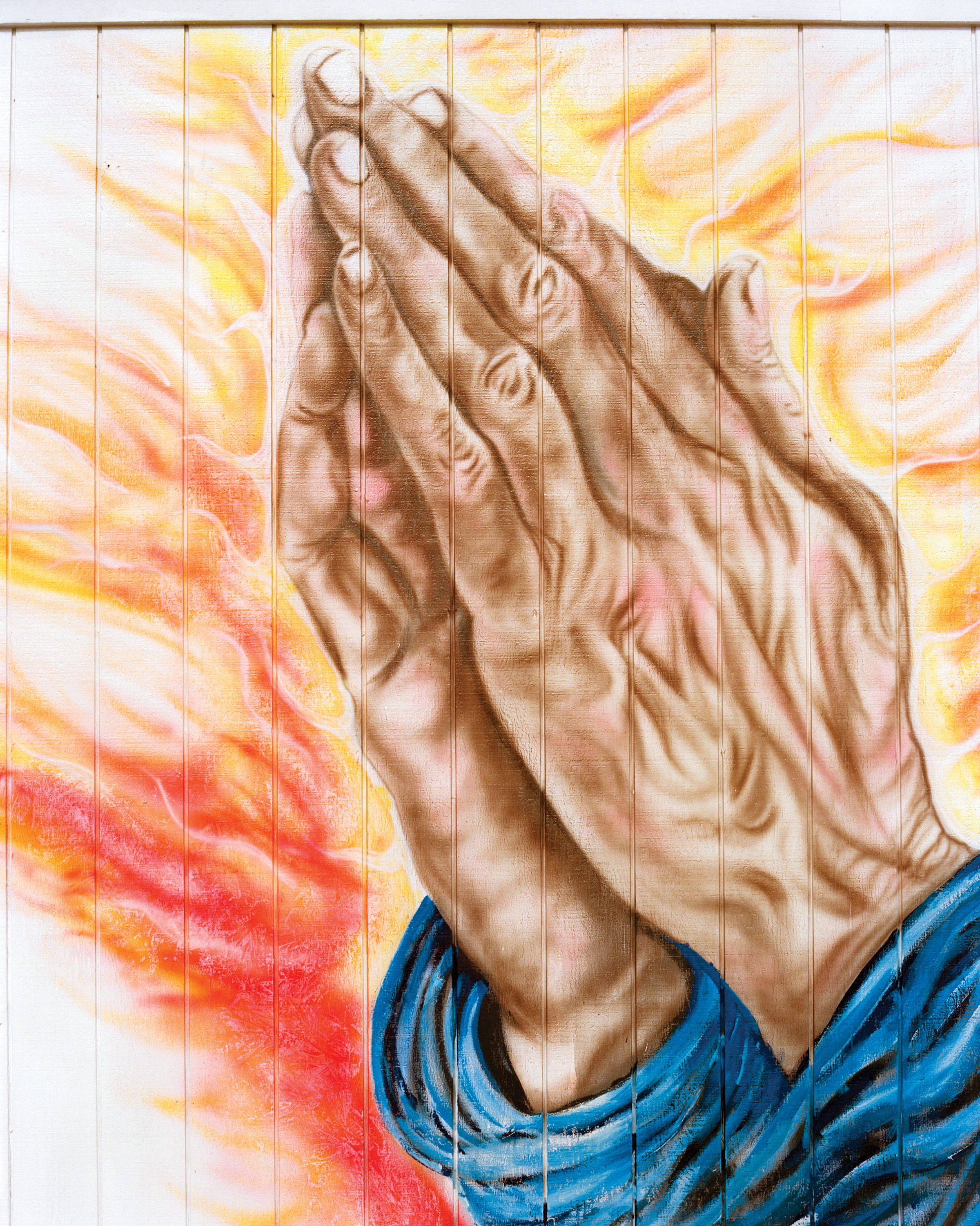 Praying hands painted across the white clapboard side of a building
