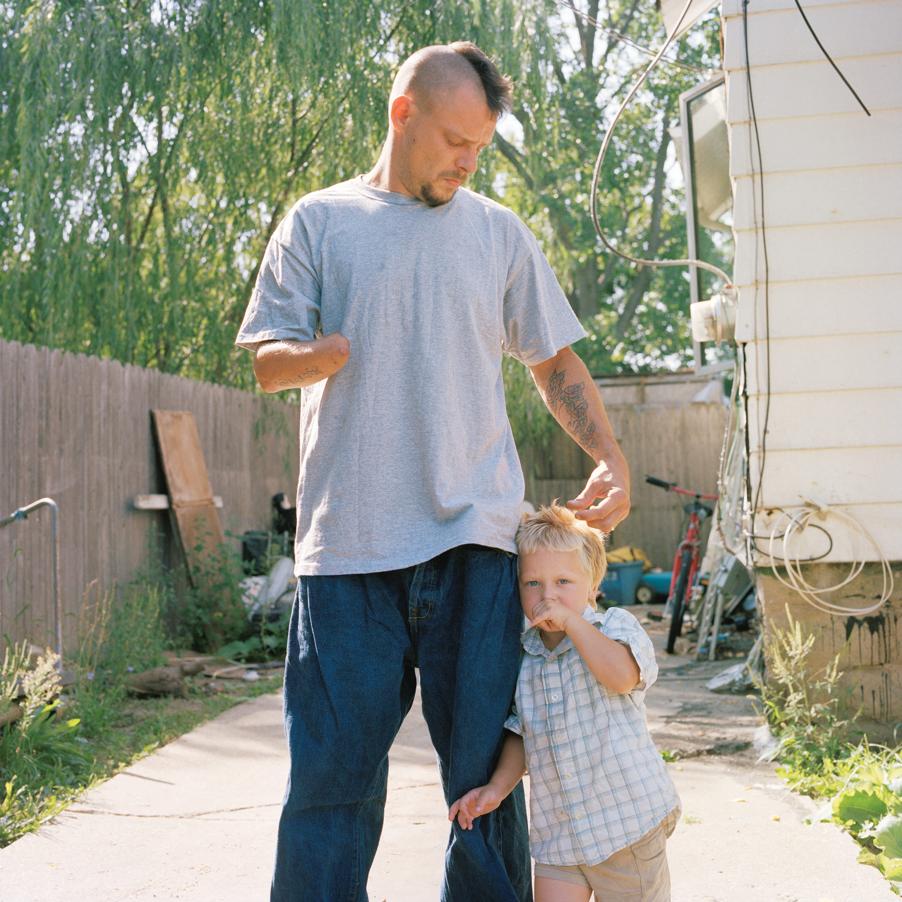 A man rests his hand on the head of a small boy in a backyard