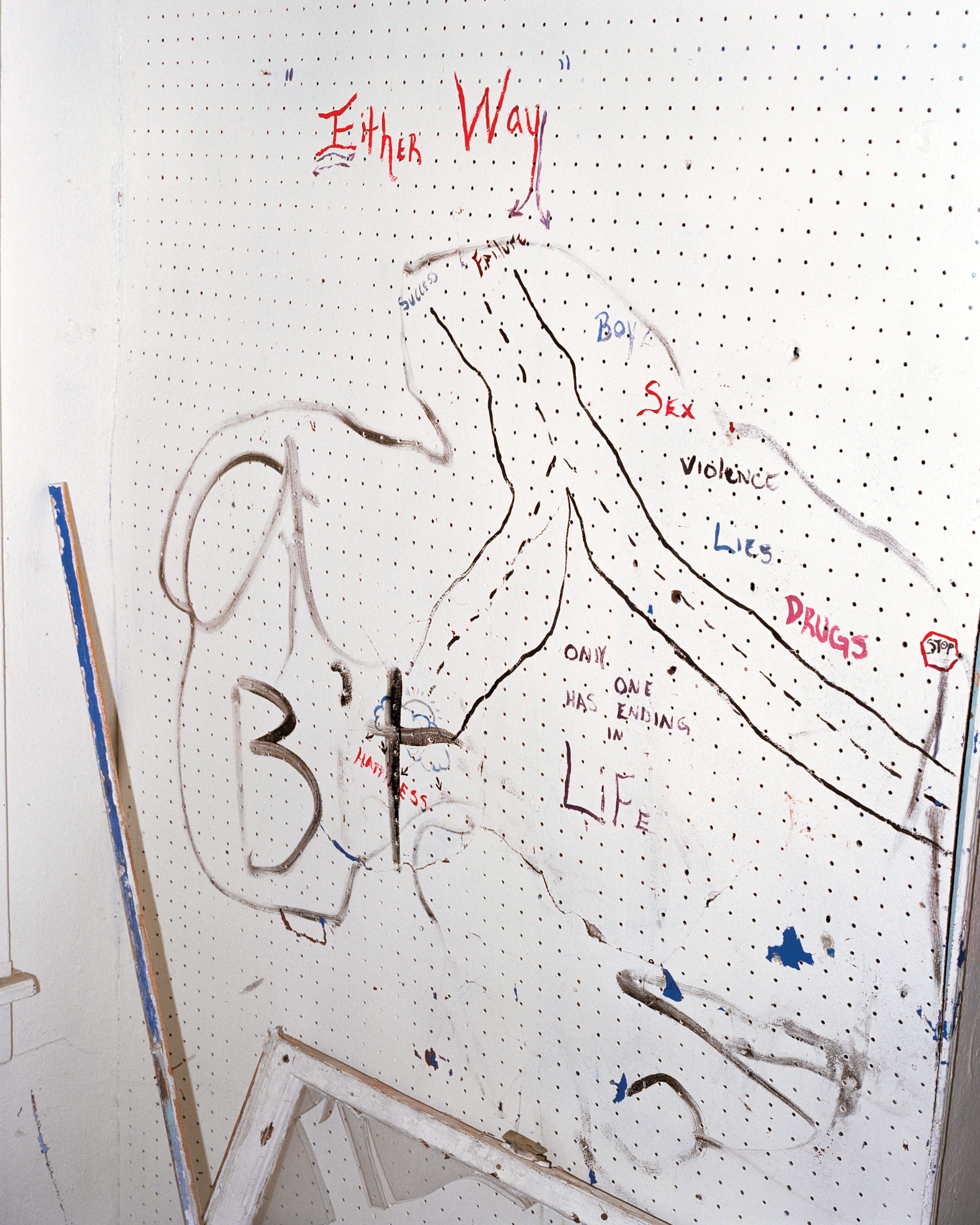 A pegboard wall marked with a chalk figure and handwritten words including Either Way and Life