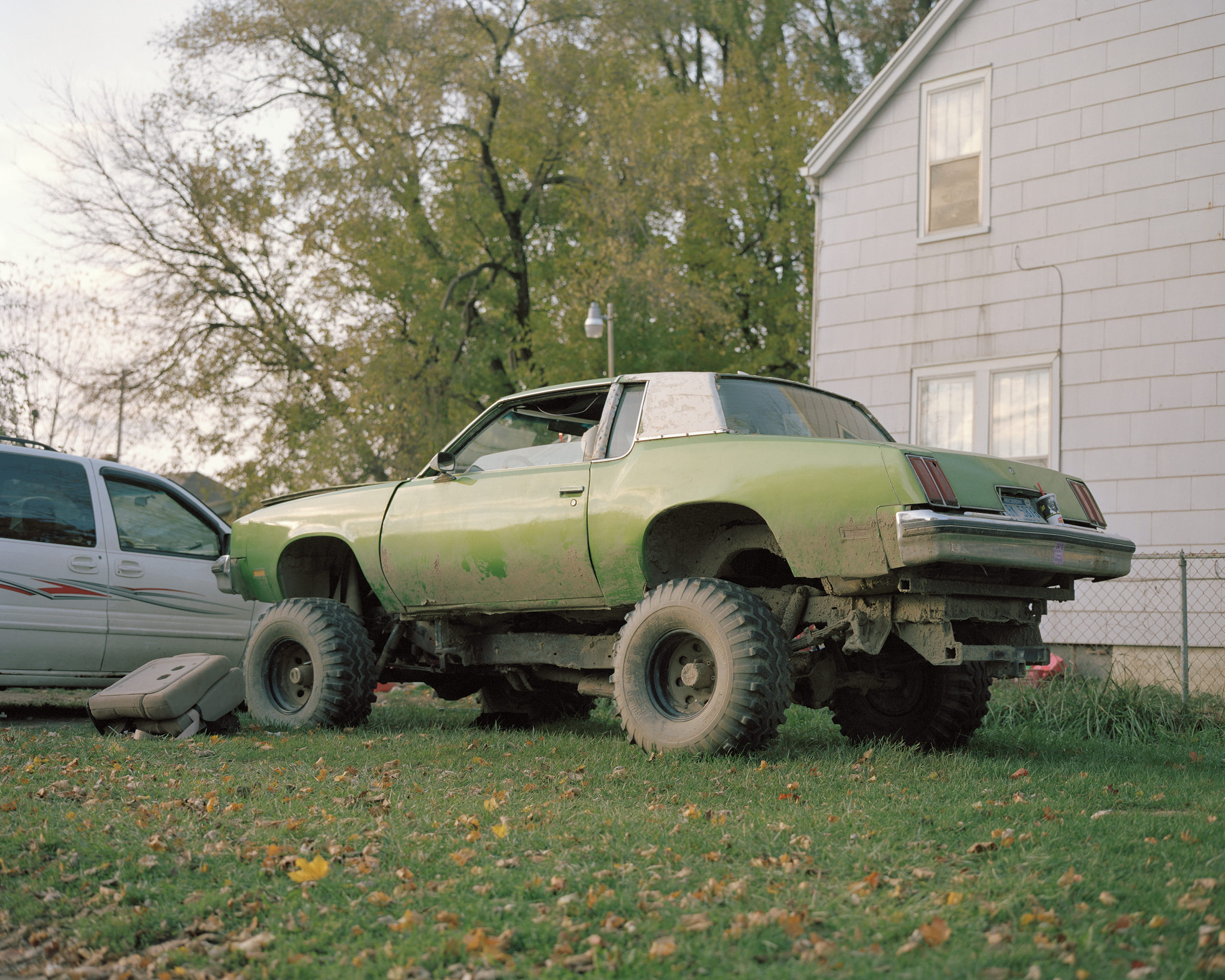 A green coupe raised on oversized off-road tires parked on a lawn